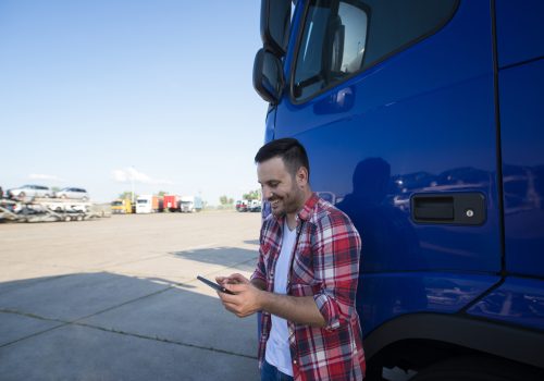 Portrait of middle aged professional trucker driver standing by his truck at truck stop using tablet computer.